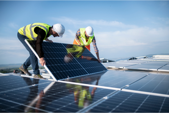 Due lavoratori con elmetti che sostengono un pannello solare su un tetto